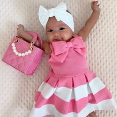 a baby doll laying on top of a bed holding a pink purse and wearing a white headband