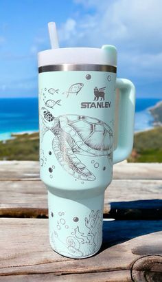 a travel mug sitting on top of a wooden table next to the ocean and sky