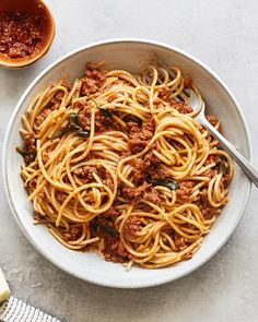 a white bowl filled with spaghetti and meat sauce next to a small bowl of parmesan cheese