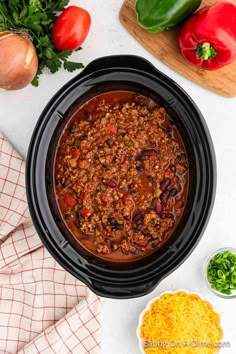 a slow cooker filled with chili and cheese next to other ingredients on a white surface