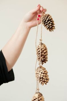 a person holding up some pine cones on a string with red nail polish and manicures