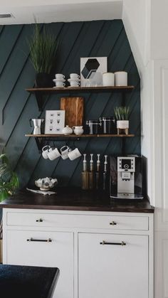 a kitchen with green walls and white cupboards, black counter top and shelves filled with items