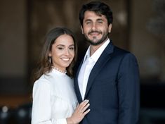 a man and woman standing next to each other in front of a building smiling at the camera