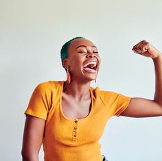 a woman in an orange shirt is raising her fist up and smiling at the camera