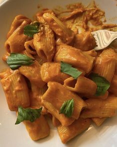 a white plate topped with pasta covered in sauce and garnished with green leaves