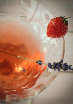 a strawberry sitting on top of a glass bowl filled with liquid and lavender sprigs