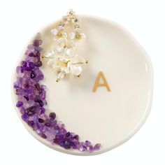 a white plate topped with purple and white flowers next to a letter shaped brooch