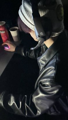 a person in a leather jacket sitting at a desk with a laptop and cup on it