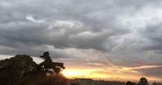 the sun is setting behind some clouds in the sky over a field with trees and buildings