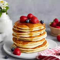 a stack of pancakes with syrup and berries on the top, next to a bowl of strawberries