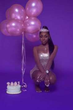 a woman kneeling next to a cake and balloons