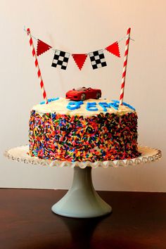 a birthday cake decorated with colorful sprinkles and race cars on the top