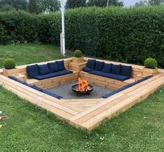 a fire pit in the middle of a lawn with blue cushions on it and some bushes