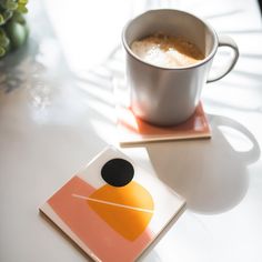 a cup of coffee sitting on top of a white table next to a square coaster