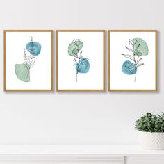 three blue and green art prints hanging on a wall above a white fireplace mantel