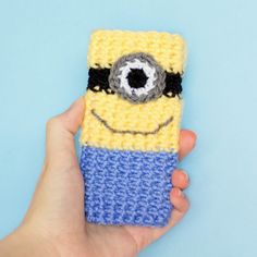 a hand holding a crocheted phone case with a minion face on it