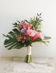 a bouquet of pink flowers and greenery on a marble countertop in front of a white wall