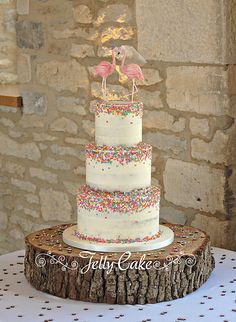 a three tiered cake with sprinkles and flamingos on top