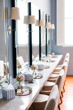 a long white table with many chairs and vases on it, along with two large mirrors