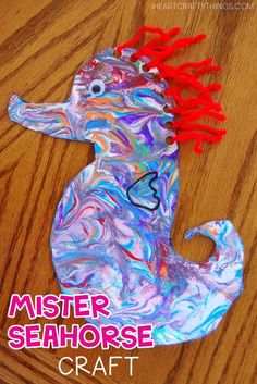 a paper plate seahorse craft with red hair on the head and tail, sitting on top of a wooden table