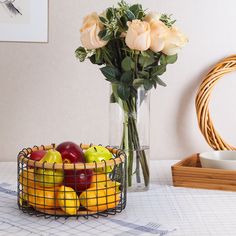 a vase filled with roses and apples next to a basket of fruit on a table