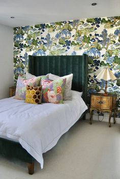 a green velvet headboard on a bed in a bedroom with floral wallpaper and lamps