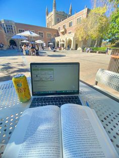 an open book sitting on top of a laptop computer next to a can of soda