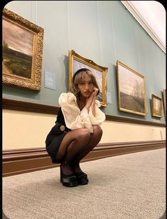 a woman sitting on the ground in front of paintings and holding her hand to her face