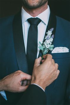 a man wearing a suit and tie adjusting the lapel flower on his boutonniere