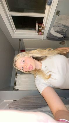 a woman with long blonde hair standing in front of an open microwave door and looking at the camera