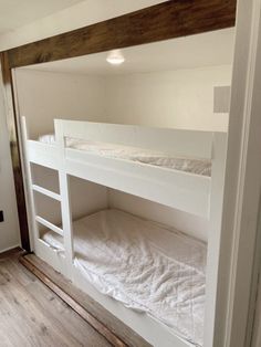 there is a bunk bed in the room with white sheets on it and wood flooring