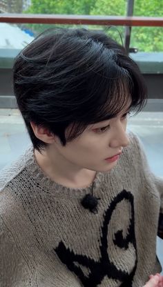 a woman with short black hair is looking at her cell phone while wearing a sweater