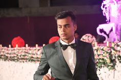 a man in a tuxedo standing next to flowers