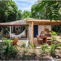 a small white house with a hammock hanging from the roof and chairs around it