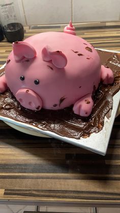 a pink pig cake sitting on top of a white plate covered in chocolate frosting