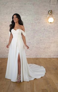 a woman in a white dress standing on a wooden floor next to a brick wall