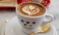 a cappuccino on a white saucer with gold spoons next to it