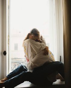 two people sitting on a window sill hugging each other