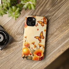 a phone case sitting on top of a wooden table next to a camera and plant