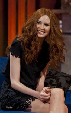 a woman with long red hair sitting on a blue couch smiling and looking at the camera