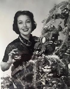 an old black and white photo of a woman decorating a christmas tree with ornaments