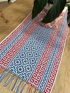 a red, white and blue table runner sitting on top of a wooden table next to a potted plant