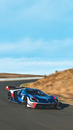 a blue and red sports car driving down the road in front of some grass on a sunny day