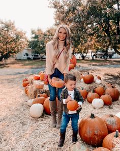 a woman and child standing in front of pumpkins