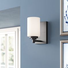 a wall light mounted on the side of a blue wall next to two framed pictures