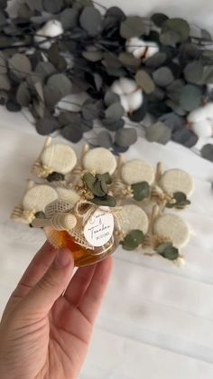 a hand holding a small bottle of honey next to a pile of leaves and branches