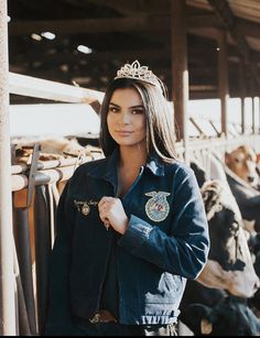 a woman wearing a tiara standing in front of cows at a dairy station with her hands on her hips