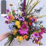 a bouquet of flowers is being held up by someone's hand in front of a white wall