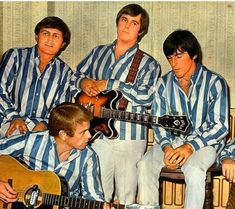 three men in blue and white striped shirts are playing the guitar while another man is sitting down