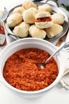 a bowl filled with red sauce next to some rolls